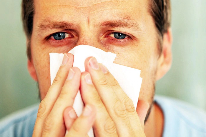 man with red eyes and tissue infront of his face